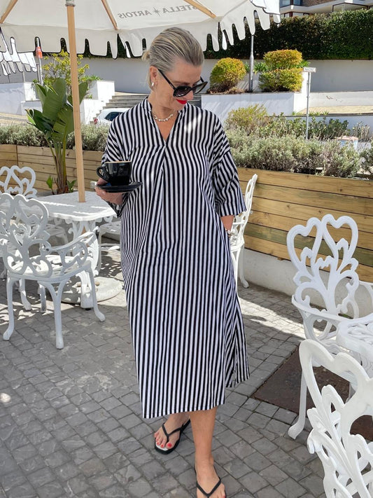 Woman in a black and white striped dress holding a coffee cup outdoors.